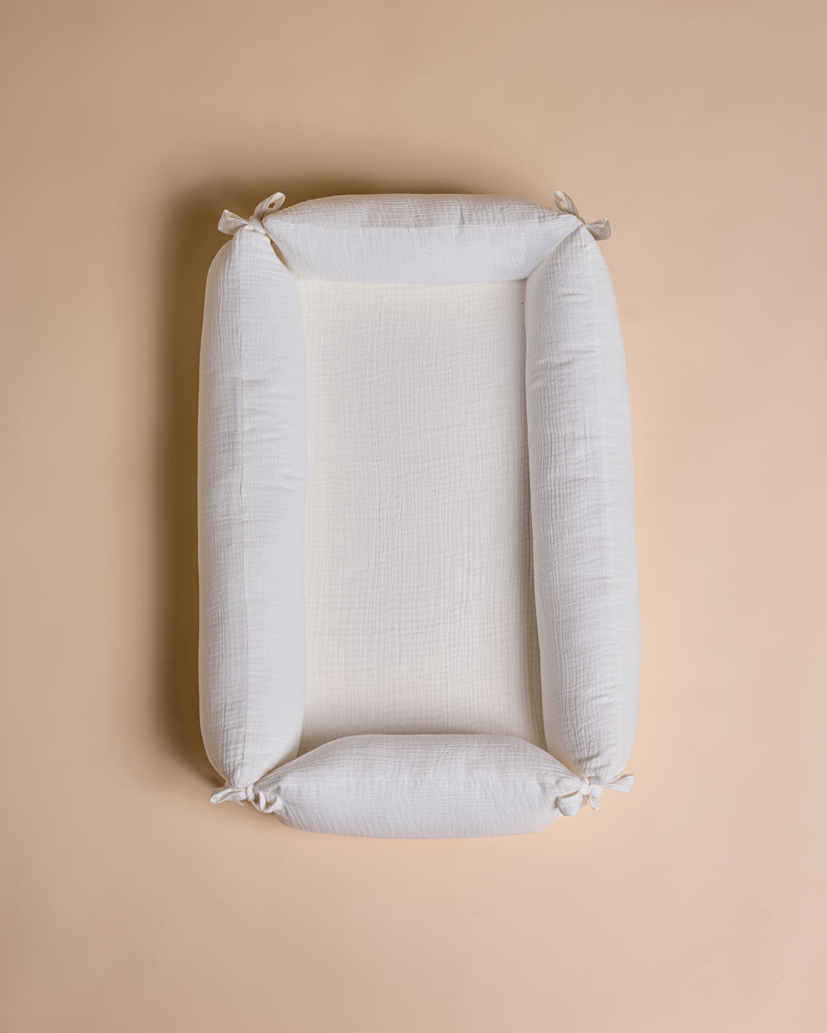 A rectangular white baby changing pad with integrated head and foot loops, shown from a top-down view on a solid beige background.