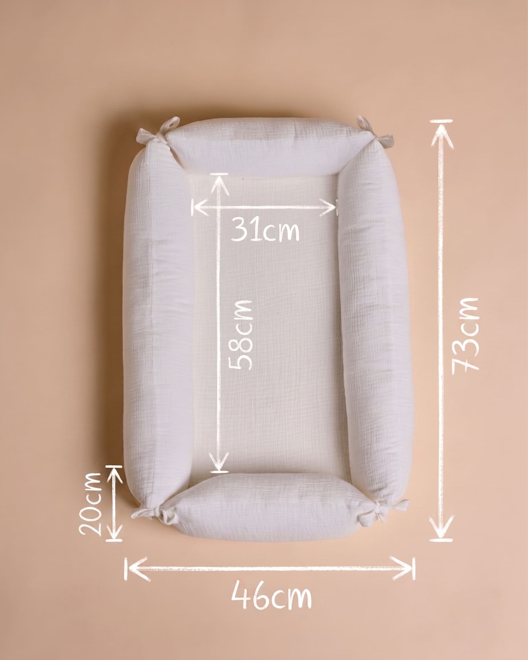 A rectangular padded baby support cushion or bassinet-style pillow shown from above on a warm beige background, with white measurement arrows and labels indicating dimensions: 73 cm tall, 46 cm wide, 31 cm inner width, 58 cm inner height, and 20 cm side depth.